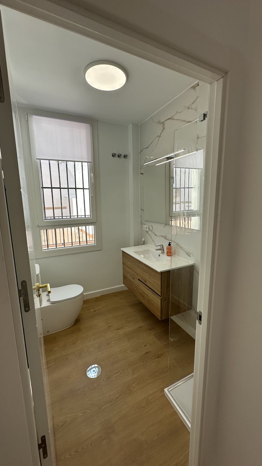 Baño reformado con mueble de madera, mampara de cristal y pared de mármol