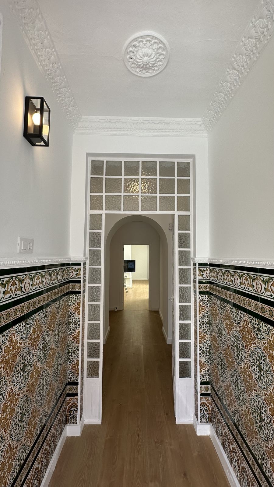 Pasillo de entrada con zócalo de azulejo sevillano, molduras restauradas y suelo de madera